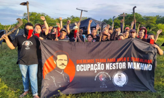 Brasilien: Foto von Landbesetzer*innen mit Transparent auf dem auf Portugiesisch Besetzung nestor Makhno steht